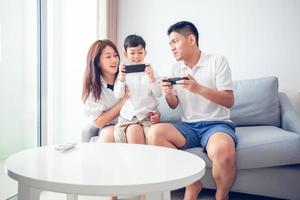 famille asiatique s'amusant à jouer à des jeux de console informatique ensemble, père et fils ont les contrôleurs du combiné et la mère encourage les joueurs. photo