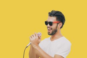 Bel homme asiatique avec une moustache, souriant et chantant au microphone isolé sur fond jaune photo