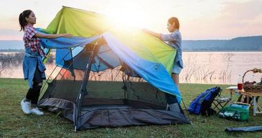 un groupe d'amis asiatiques touristes buvant et jouant de la guitare avec bonheur en été tout en campant près du lac au coucher du soleil photo