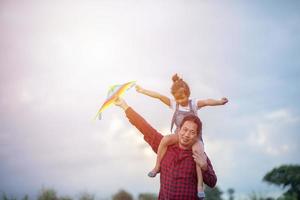 fille et père d'enfant asiatique avec un cerf-volant courant et heureux sur le pré en été dans la nature photo