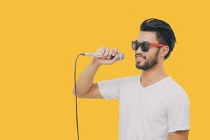 Bel homme asiatique avec une moustache, souriant et chantant au microphone isolé sur fond jaune photo