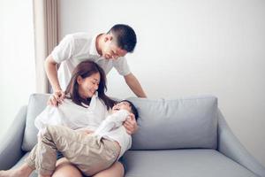 famille asiatique heureuse avec son fils à la maison sur le canapé jouant et riant photo