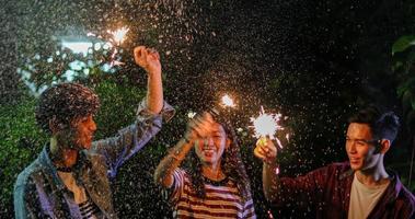 groupe d'amis asiatiques ayant un barbecue de jardin en plein air riant avec des boissons alcoolisées à la bière et montrant un groupe d'amis s'amusant avec des cierges magiques la nuit photo