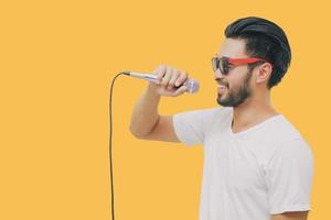 Bel homme asiatique avec une moustache, souriant et chantant au microphone isolé sur fond jaune photo