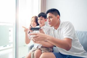 famille asiatique s'amusant à jouer à des jeux de console informatique ensemble, père et fils ont les contrôleurs du combiné et la mère encourage les joueurs. photo