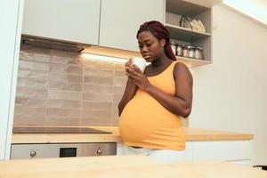 femme enceinte noire prenant une tasse de café à la cuisine photo