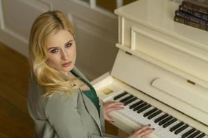 belle blonde joue du piano dans un costume gris.