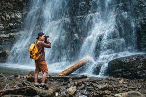 homme voyageur avec un sac à dos jaune debout sur fond d'une cascade fait un paysage photo