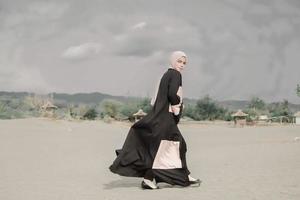 beau modèle féminin islamique portant la mode hijab, une robe de mariée moderne pour femme musulmane se promène le long du sable et de la mer. un modèle de fille asiatique utilisant le hijab s'amusant à la plage. photo avant mariage