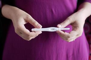 main de femme tenant un kit de test de grossesse sur un bureau en bois. photo