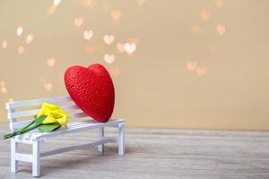 coeur rouge avec un bouquet de lys jaunes sur un banc blanc sur fond de bokeh. concept d'amour, gros plan avec espace de copie. photo