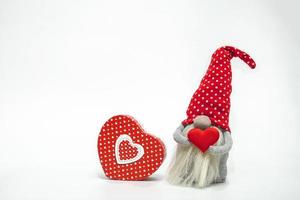 lutin dans un chapeau rouge avec un coeur rouge dans ses mains et une boîte cadeau isolée sur fond blanc. idée saint valentin photo