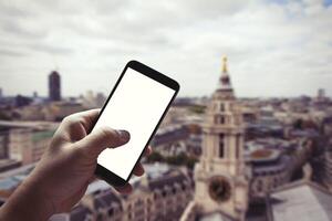 main d'homme tenant un smartphone à écran blanc contre l'arrière-plan flou de la ville de Londres photo