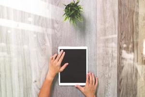 main d'homme d'affaires travaillant avec une tablette numérique. sur un bureau en bois avec plante. vue de dessus. effets de double exposition, minimalisme photo