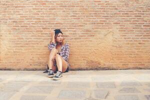 jeune femme triste assise contre le mur de briques seul. photo