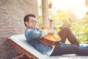 de beaux hommes hipster s'entraînent à jouer de la guitare pendant qu'il profite de la détente avec la nature environnante. photo