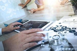 docteur en médecine main travaillant avec un ordinateur moderne et une tablette numérique pro avec son équipe avec un diagramme médical numérique sur un bureau en bois comme concept médical photo