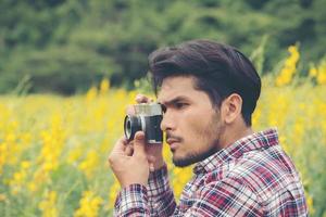 jeune bel homme hipster photographier avec un appareil photo rétro avec champ de fleurs jaune nature.