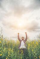 bel homme hipster debout levant les mains en l'air dans un champ de fleurs jaunes. photo