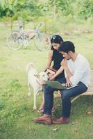 jeune couple d'éducation assis sur le banc jouer avec un chien à l'extérieur et par beau temps. et ils sont heureux, concept de style de vie. photo