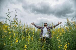 bel homme hipster debout levant les mains en l'air dans un champ de fleurs jaunes. photo