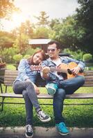 jeune couple amoureux jouant de la guitare acoustique dans le parc tout en étant assis sur le banc ensemble. photo