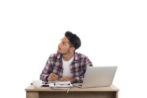 jeune homme réfléchi regardant loin tout en étant assis sur son lieu de travail isolé sur fond blanc. photo