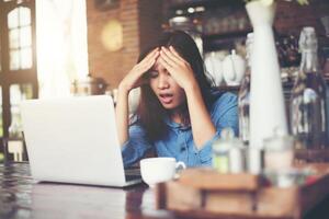 jeune femme assise dans un café avec son ordinateur portable, stressante pour le travail. photo