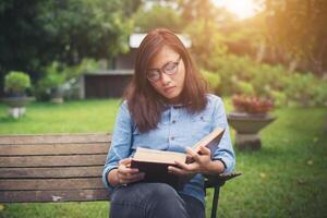 hipster charmante fille se détendre dans le parc tout en lisant un livre, profiter de la nature autour. photo