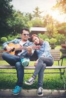 jeune couple amoureux jouant de la guitare acoustique dans le parc tout en étant assis sur le banc ensemble. photo