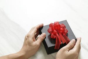 cadeaux, main d'homme tenant une boîte cadeau dans un geste de donner sur fond de table en marbre gris blanc photo