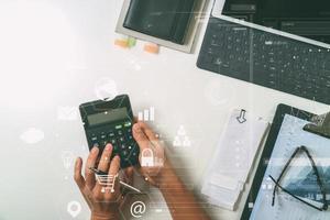 vue de dessus de la main d'homme d'affaires travaillant avec les finances sur le coût et la calculatrice et latop avec téléphone portable sur le bureau blanc dans un bureau moderne avec diagramme d'icône vr photo