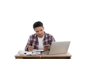 homme d'affaires regardant son téléphone tout en travaillant avec un ordinateur portable au bureau isolé sur fond blanc. photo