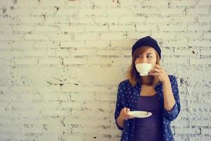 belle femme buvant du café sur fond de mur de briques blanches photo