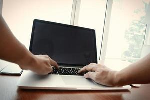 Gros plan de la main de l'homme d'affaires travaillant sur un ordinateur portable à écran blanc sur un bureau en bois comme concept photo