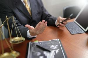 concept de justice et de droit. avocat masculin au bureau avec le marteau, travaillant avec un téléphone intelligent, un clavier d'accueil pour tablette numérique, une balance en laiton, sur une table en bois