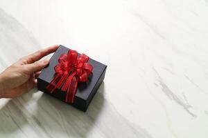 cadeaux, main d'homme tenant une boîte cadeau dans un geste de donner sur fond de table en marbre gris blanc photo