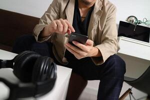 jeune homme est assis sur un canapé faisant du shopping en ligne écoute de la musique avec des écouteurs tient un smartphone sur sa main à la maison, concept omni channel photo