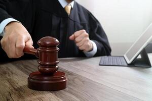 concept de justice et de droit. juge masculin dans une salle d'audience frappant le marteau, travaillant avec un clavier d'accueil d'ordinateur tablette numérique sur une table en bois photo