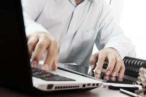 main d'homme d'affaires travaillant avec une tablette numérique et un ordinateur portable sur un bureau en bois au bureau photo