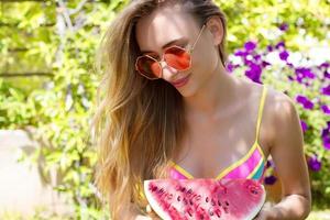 gros plan d'une fille heureuse dans des lunettes de soleil roses et des fruits de pastèque. vacances d'été et week-end amusant. notion d'été. souriante jeune femme en maillot de bain fashion. mise au point sélective. tenue d'été de plage. photo