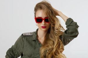 visage de femme gros plan dans des lunettes de soleil rouges isolés sur fond blanc. fille en chemise, maquillage des lèvres rouges. concept de beauté de mode. belle peau de visage et accessoires à la mode. cheveux longs style glamour photo