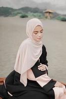 beau modèle féminin islamique portant la mode hijab, une robe de mariée moderne pour femme musulmane assise dans le sable et la plage. portrait d'une fille asiatique modèle utilisant le hijab s'amusant à la plage avec des arbres photo