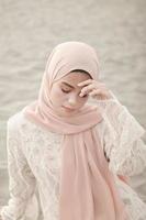 beau modèle féminin islamique portant la mode hijab, une robe de mariée moderne pour femme musulmane assise dans le sable et la plage. portrait d'une fille asiatique modèle utilisant le hijab s'amusant à la plage avec des arbres photo