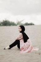 beau modèle féminin islamique portant la mode hijab, une robe de mariée moderne pour femme musulmane assise dans le sable et la plage. portrait d'une fille asiatique modèle utilisant le hijab s'amusant à la plage avec des arbres photo