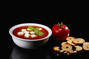 Soupe à la tomate. soupe de tomates maison avec morceaux de mozzarella, tomates, herbes, épices et basilic frais. avec des bruschettas grillées sur le côté. photo