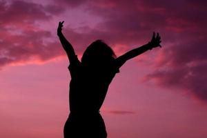 une femme heureuse et forte en confiance ouvre les bras et saute sous le magnifique coucher de soleil photo