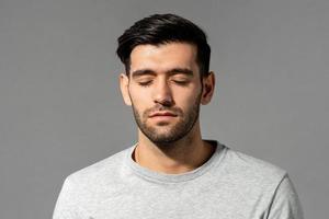 portrait en gros plan d'un jeune homme caucasien serein face aux yeux fermés sur fond de studio gris clair isolé photo