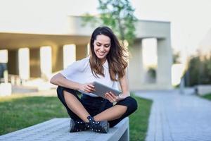 femme d'âge moyen utilisant une tablette numérique assise à l'extérieur en milieu urbain. photo