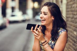 jeune femme souriante enregistrant une note vocale dans son téléphone intelligent